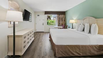 A hotel room with a bed, a dresser, a television, and a window with curtains.