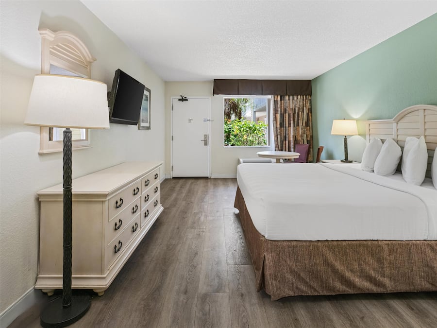 A hotel room with a bed, a dresser, a television, and a window with curtains.