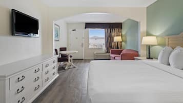A hotel room with a bed, a TV mounted on the wall, a desk, a chair, and a window with curtains.