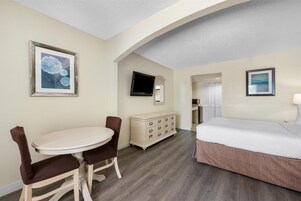 Una habitación de hotel con cama, una mesa de comedor con sillas, un aparador y un televisor en la pared.