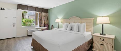 A neatly arranged hotel room with a large bed, bedside tables with lamps, a wardrobe, and a window with curtains.