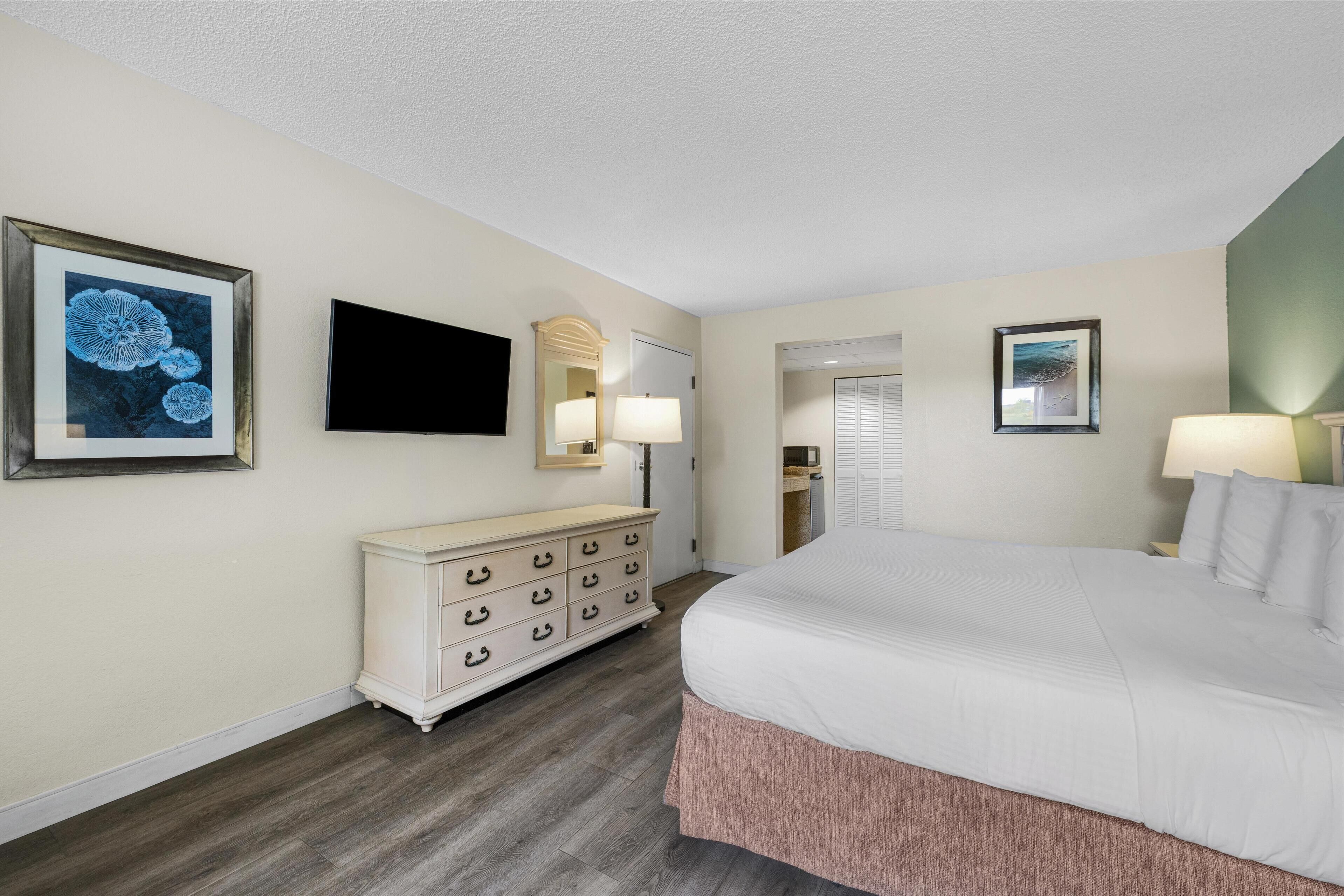 A hotel room with a large bed, a dresser, a television, and framed artwork on the walls.