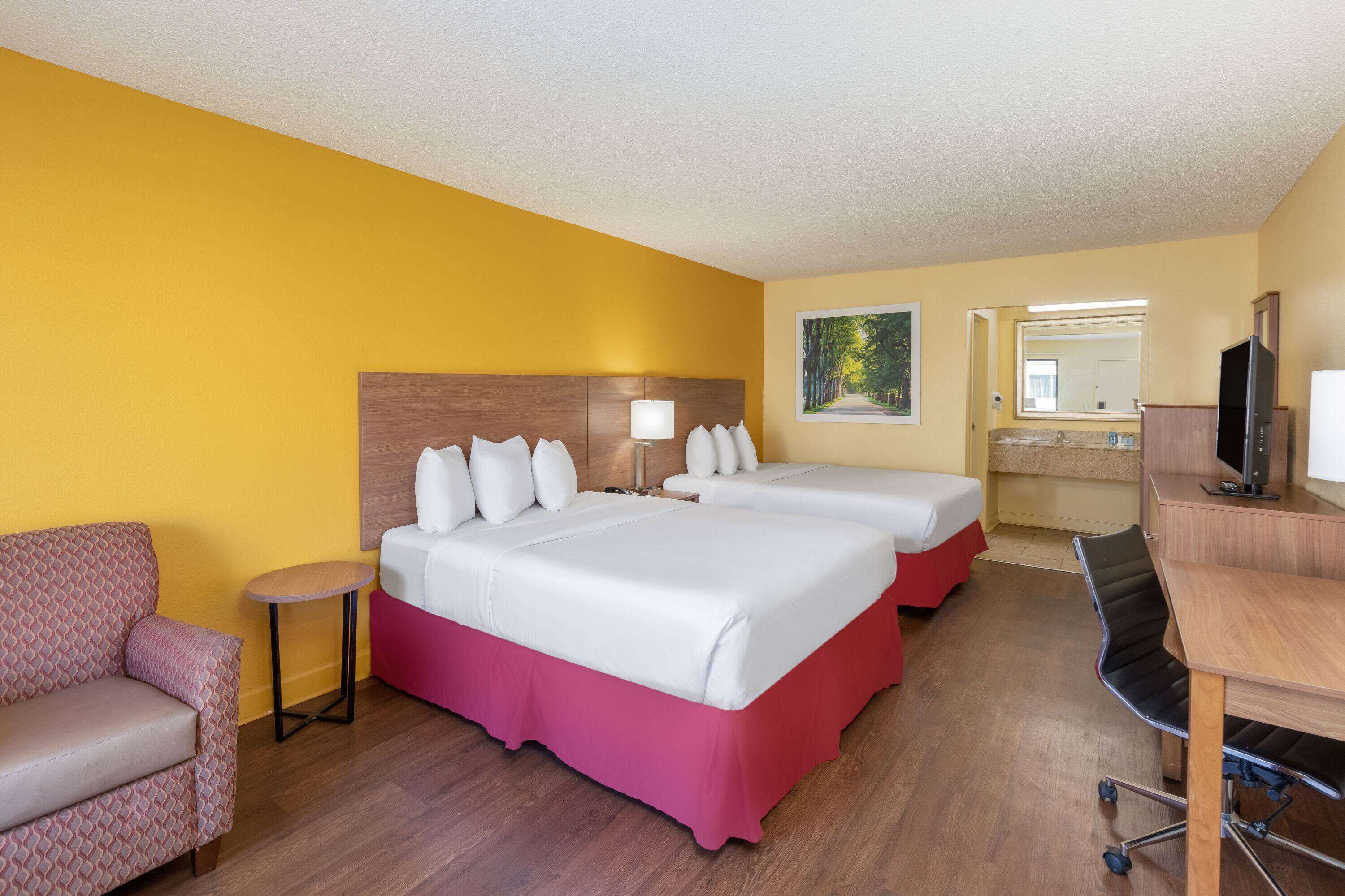 A hotel room with two beds, a desk, a chair, a TV, and a painting on the wall.