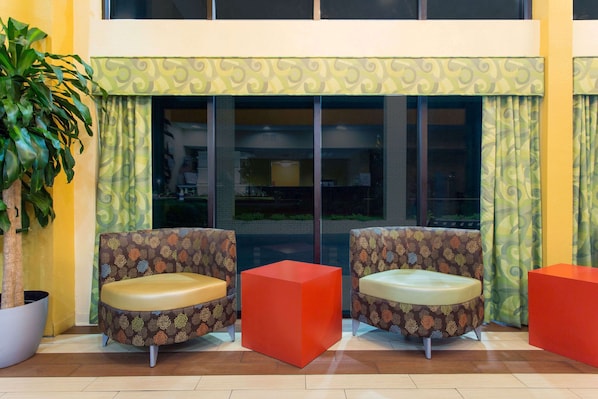 A seating area with two patterned chairs and a red cube, a potted plant, and a yellow wall. - Days Inn by Wyndham Florence/I-95 North (Florence)