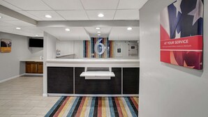 A reception area with a modern design, featuring a counter, a colorful striped carpet, and a poster on the wall. - Motel 6 Carlisle, PA - Cumberland Valley (Carlisle)