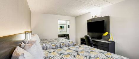 A hotel room with two beds, a desk, a chair, a TV, and a mirror.