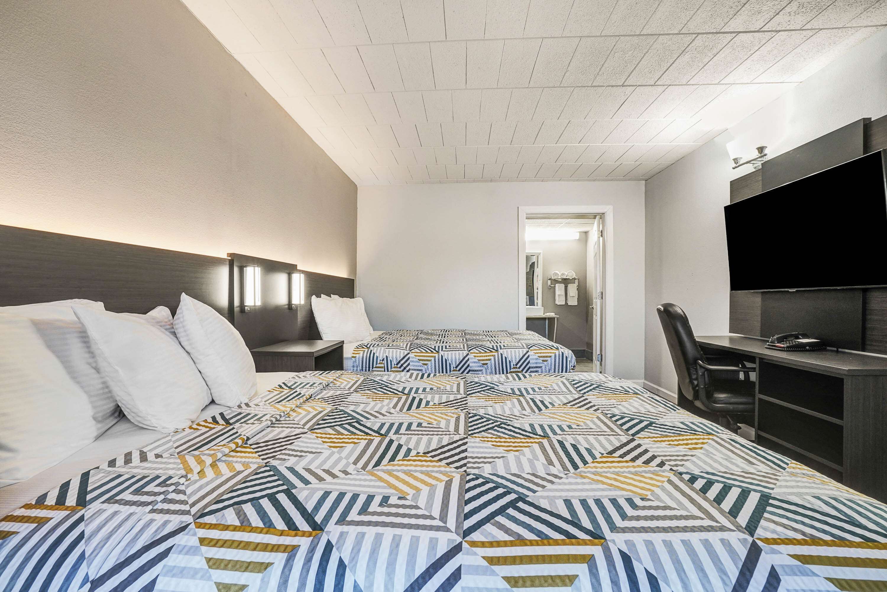 A hotel room with a large bed, a desk, a chair, a TV, and a door leading to a bathroom.