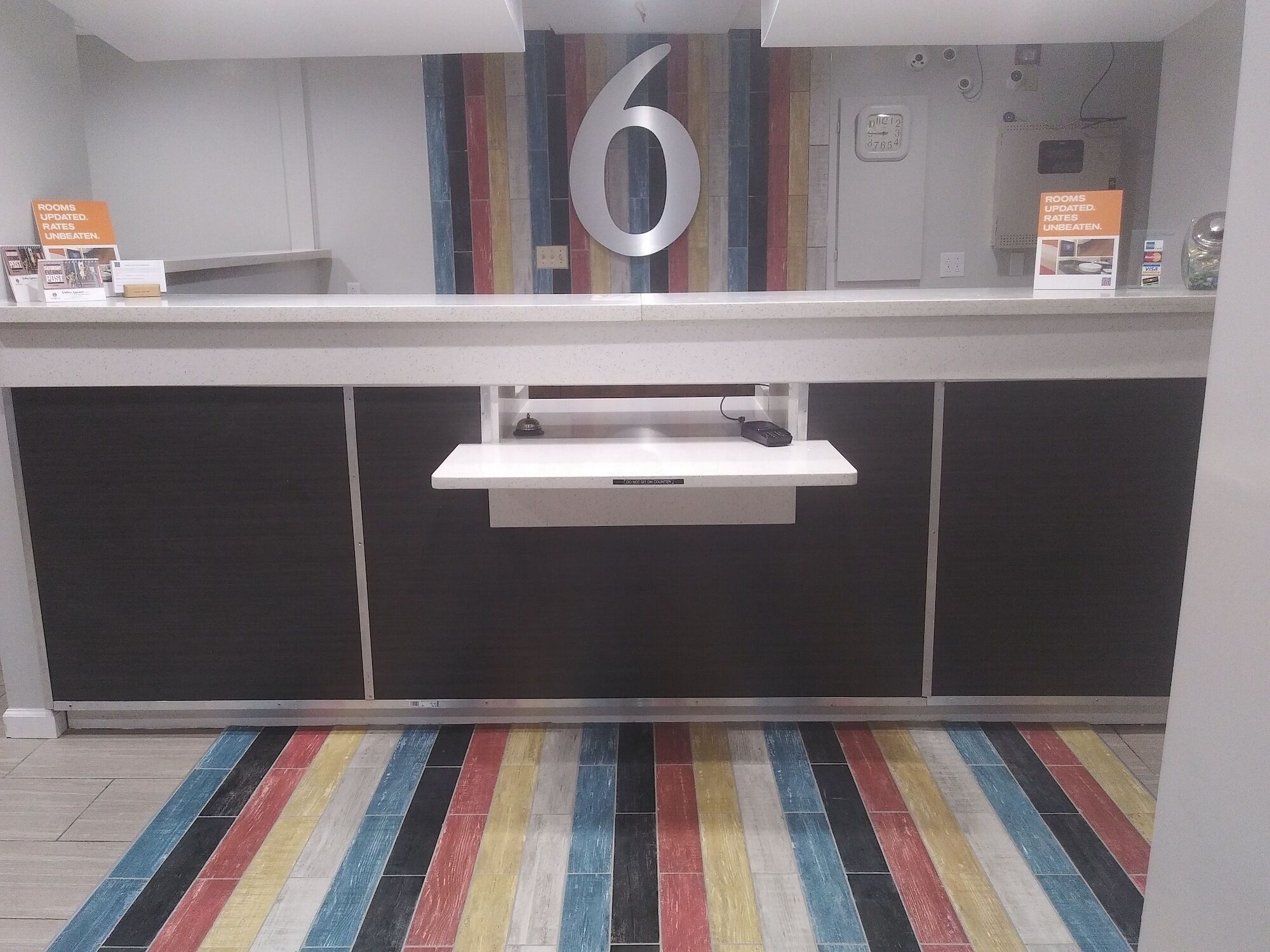 Een receptiebalie met daarboven een bord met het cijfer '6', een klok en een bordje met actuele kamerprijzen.