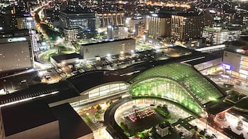 Um hotel moderno com fachada de vidro curva, estacionamento e paisagem urbana ao redor, à noite.