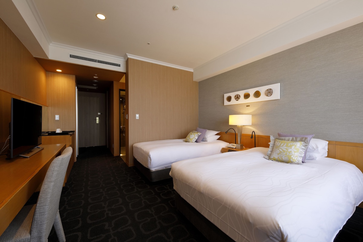 Habitación de hotel con dos camas, un escritorio, un televisor y una lámpara.