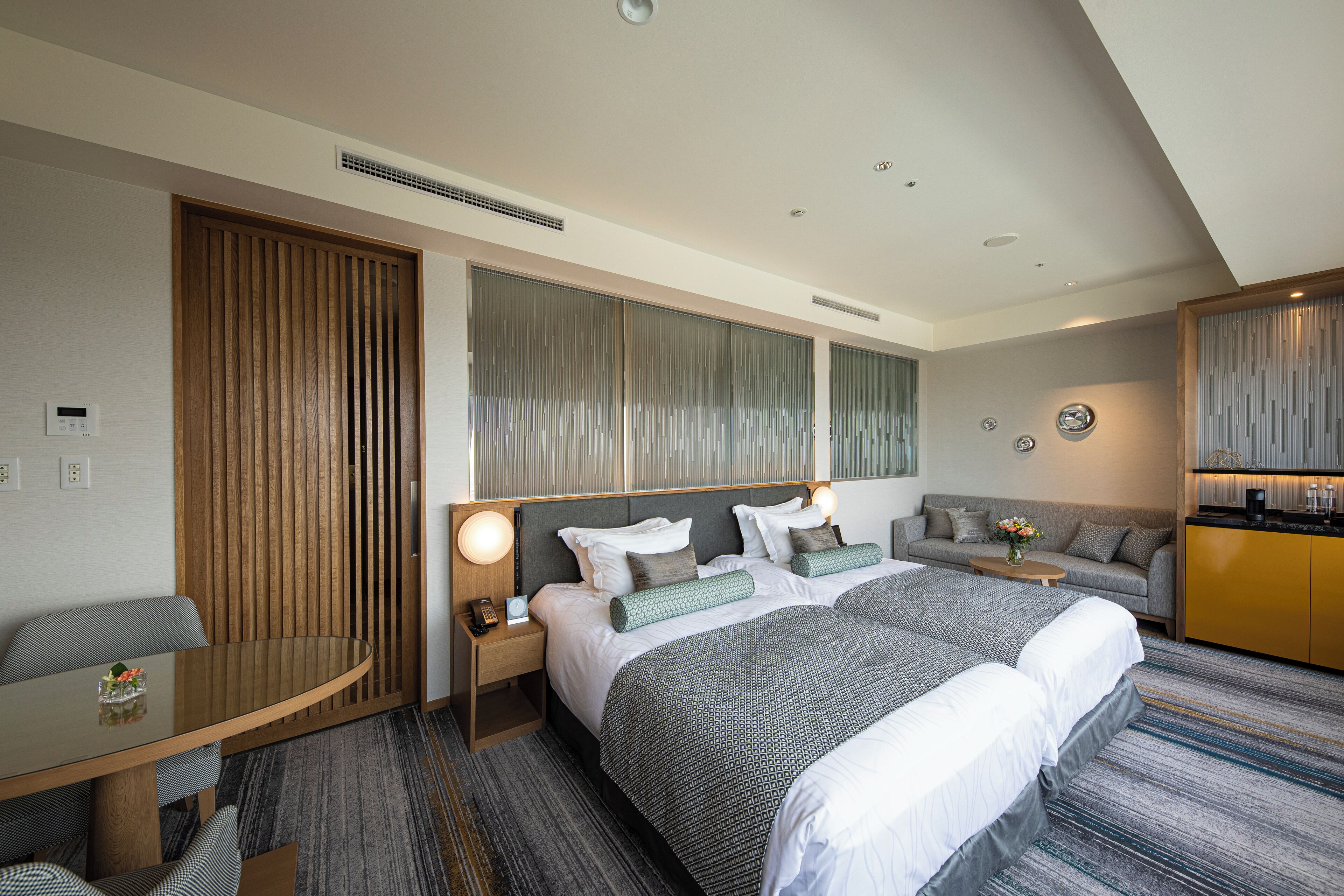 A hotel room with two beds, a sofa, a dining table, and a kitchenette.