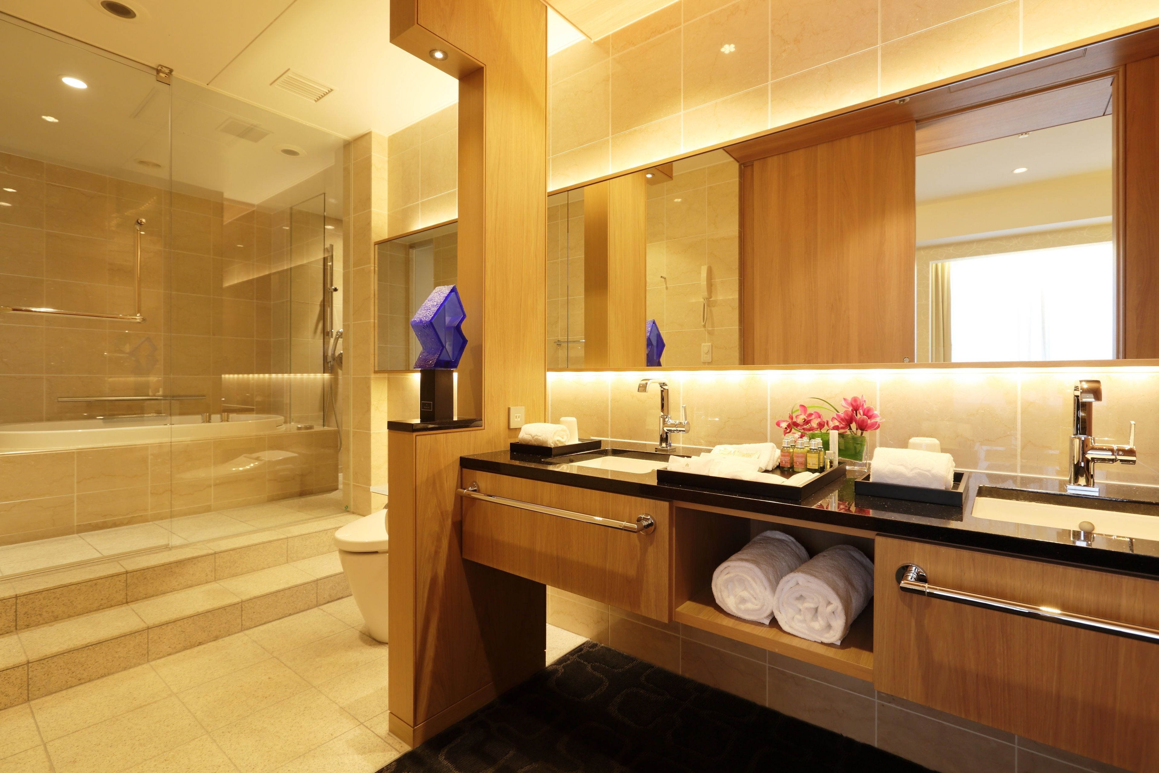 A modern bathroom with a glass-enclosed shower, a vanity with a large mirror, and neatly folded towels.