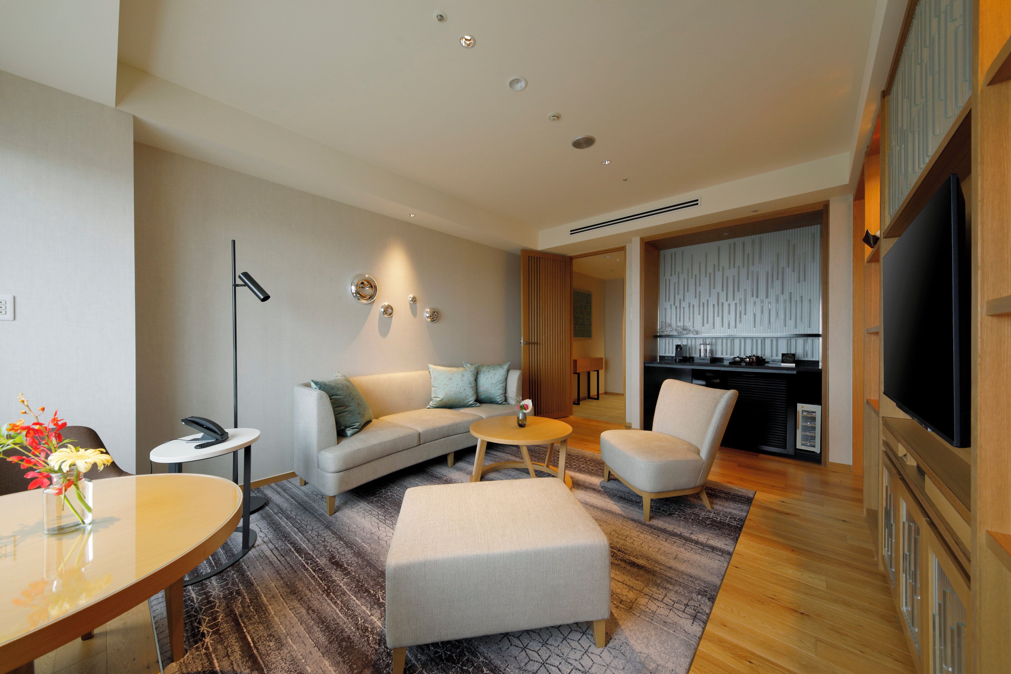 A modern living room with a sofa, ottoman, coffee table, and a dining table with a vase of flowers.