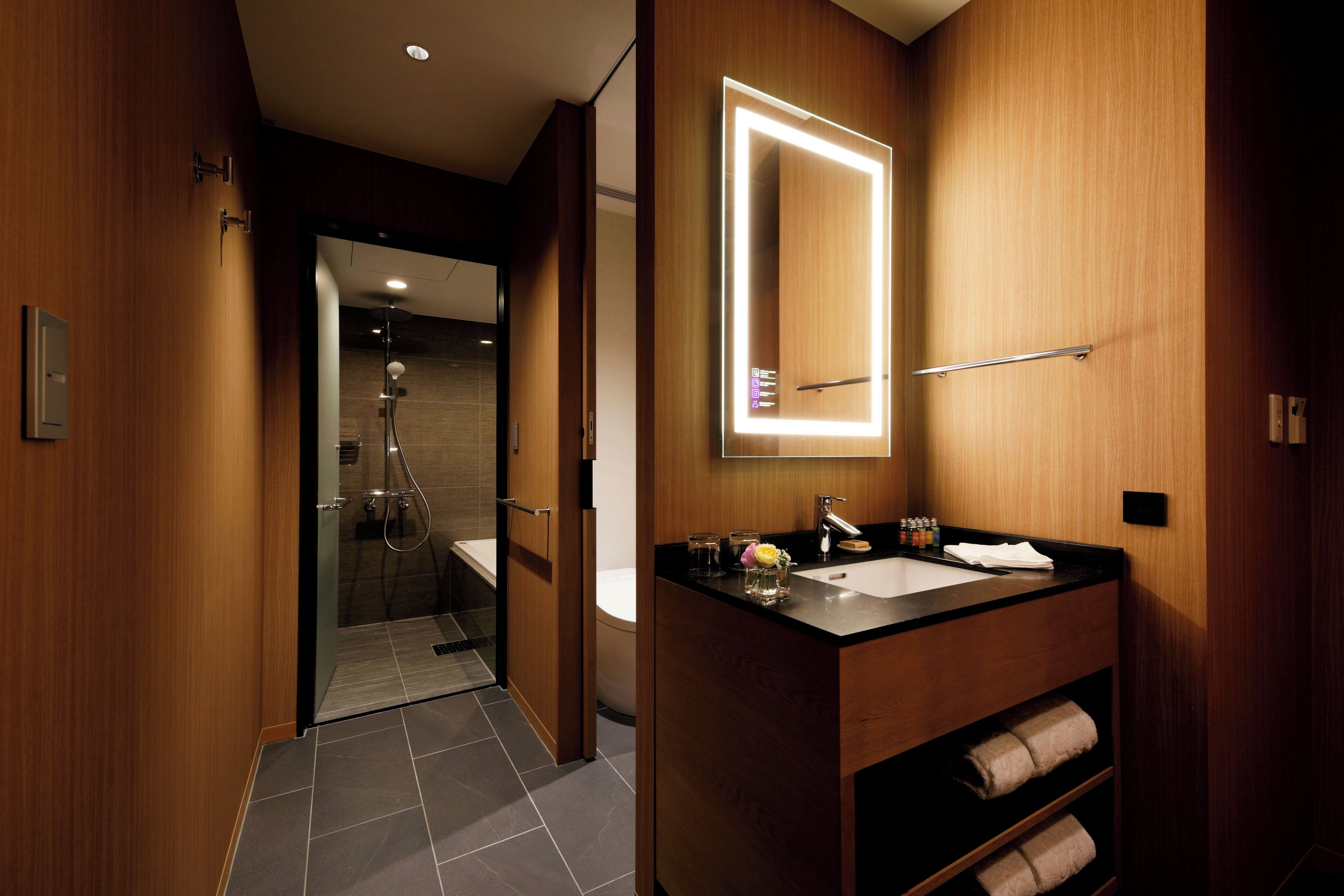 Un baño moderno con tocador de madera, un espejo grande y zona de ducha.