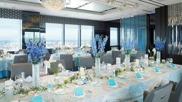 Un salón de banquetes con mesas redondas dispuestas para un evento formal, con centros de mesa florales y vistas a la ciudad.
