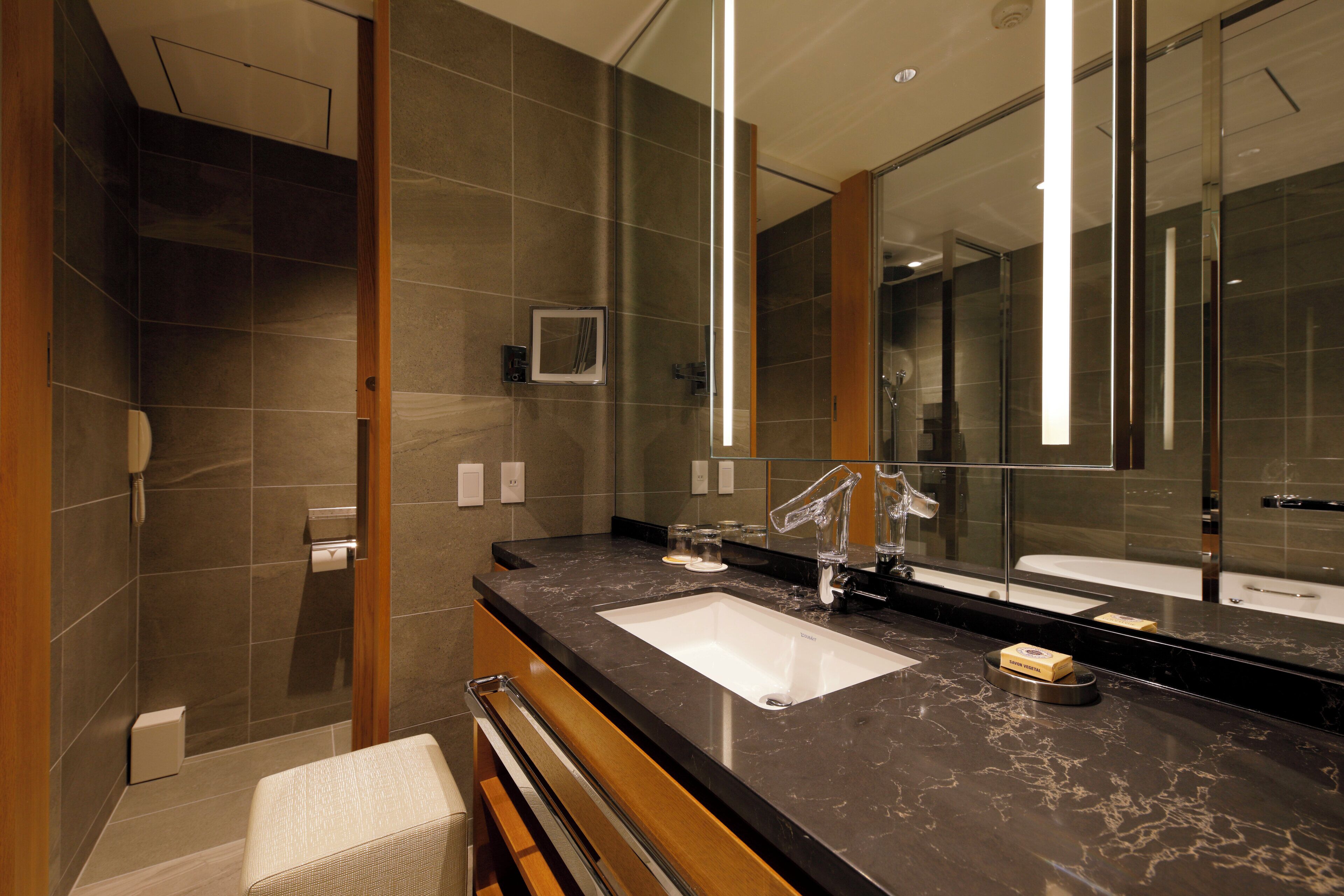 A modern bathroom with a large mirror, two sinks, and a shower area.