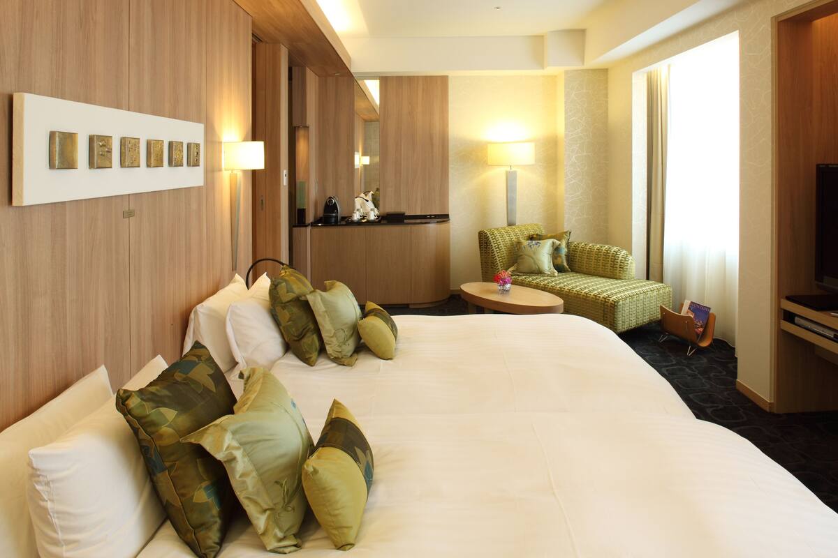 A hotel room with a large bed, a seating area with a chair and a small table, a television, and a mirror.