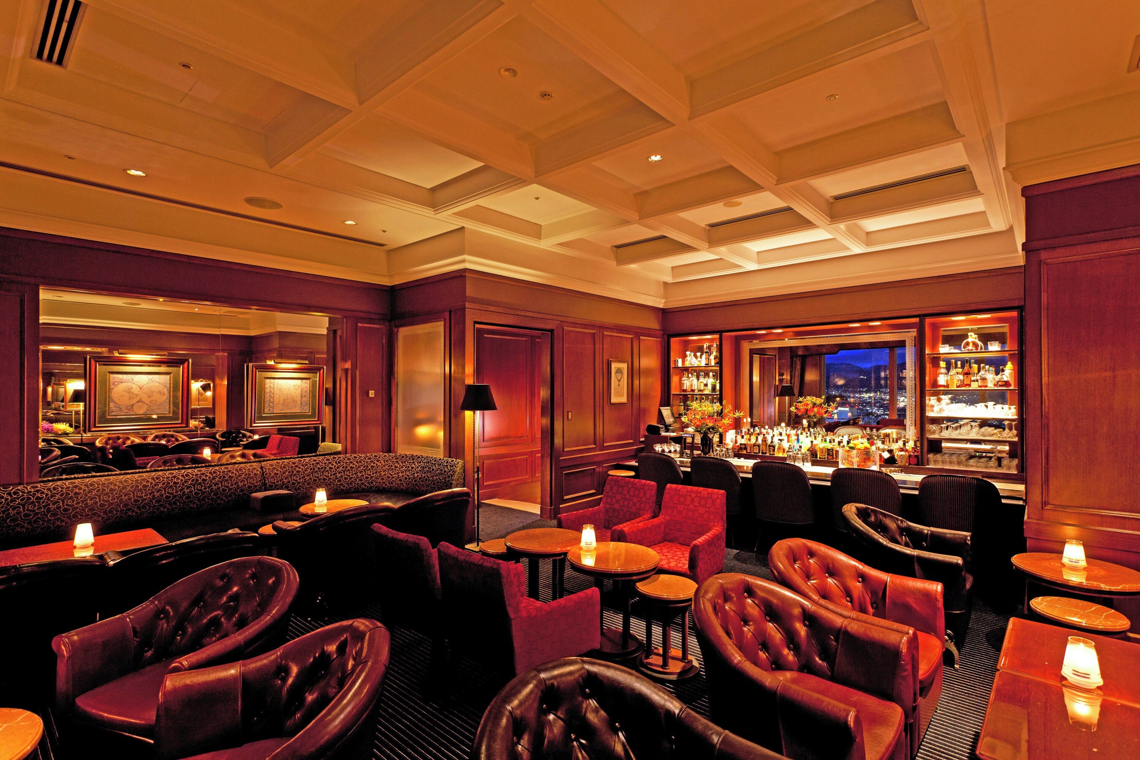 A bar area with leather seating, a bar counter, and a view of the city at night.