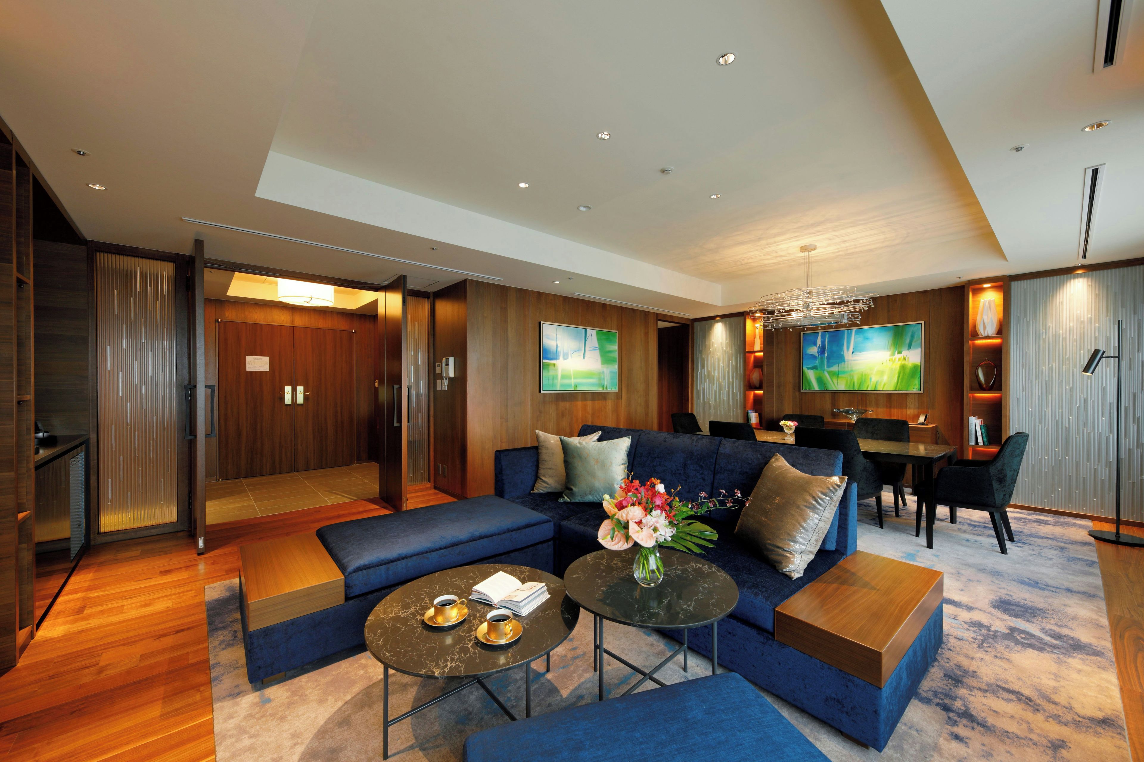 A modern hotel lobby with a blue sofa, a coffee table, and a dining area with a chandelier.