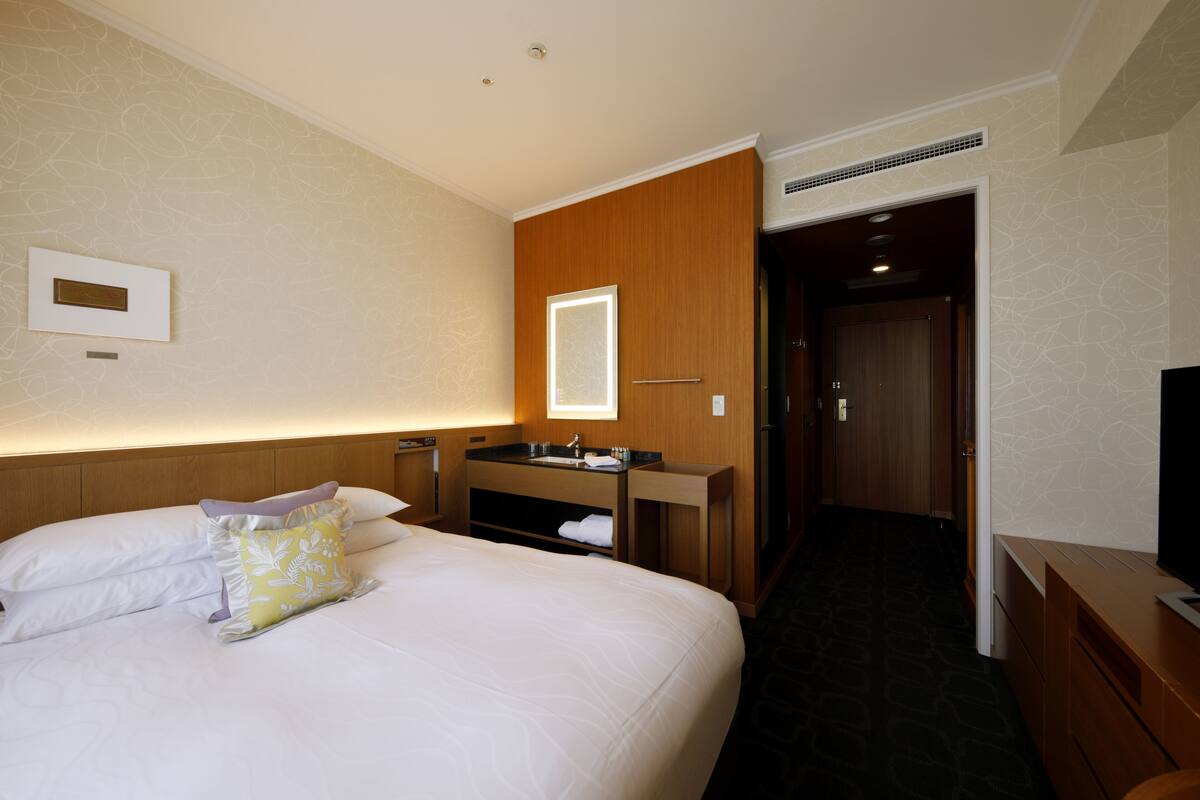 A hotel room with a large bed, a wooden wardrobe, a built-in vanity with a mirror, and a television on a wooden dresser.