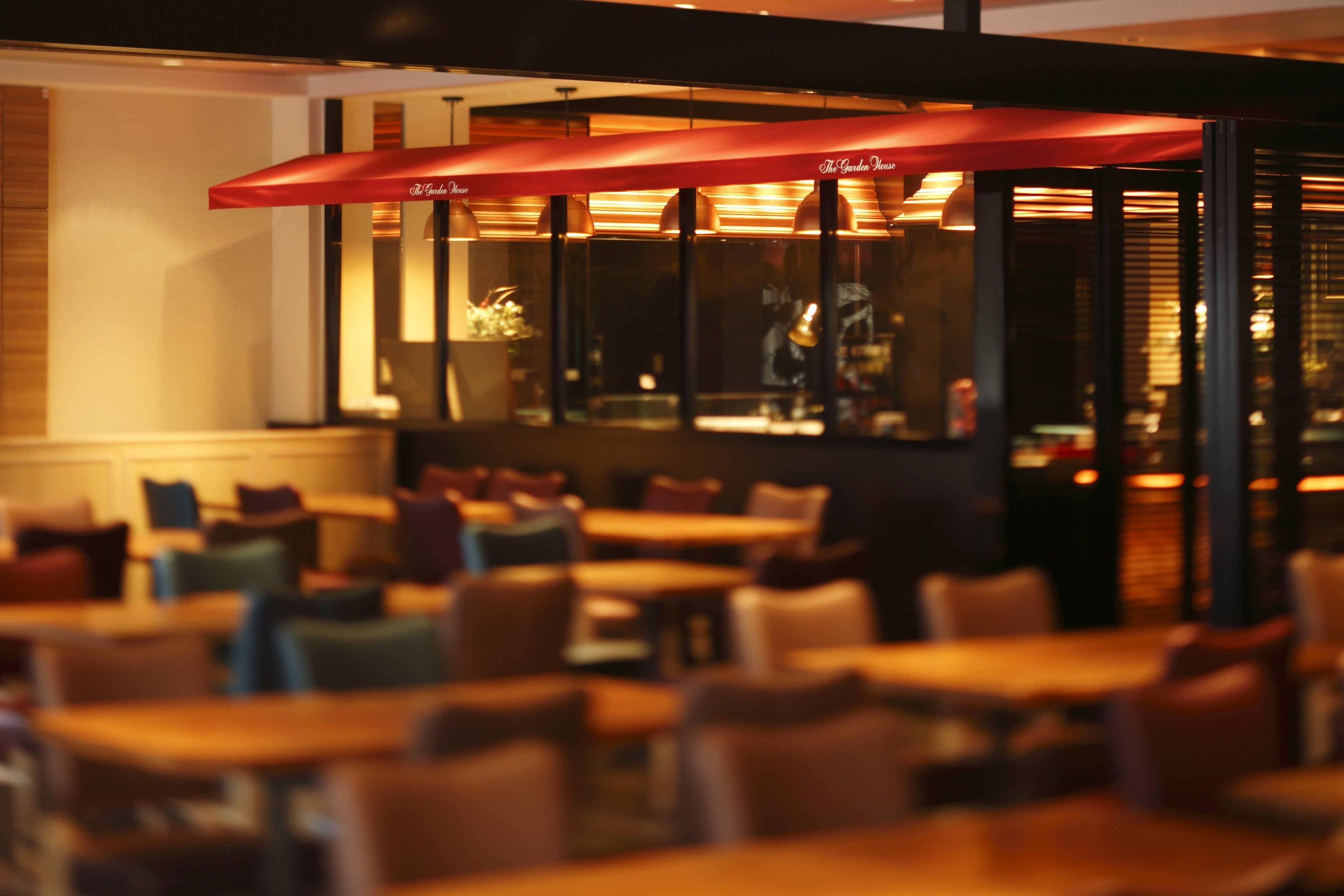 A restaurant with tables and chairs, red umbrellas, and a view of the street outside.