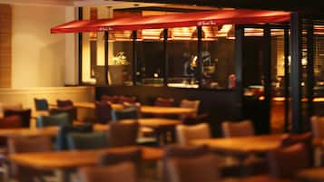 A restaurant with tables and chairs, red umbrellas, and a view of the street outside.
