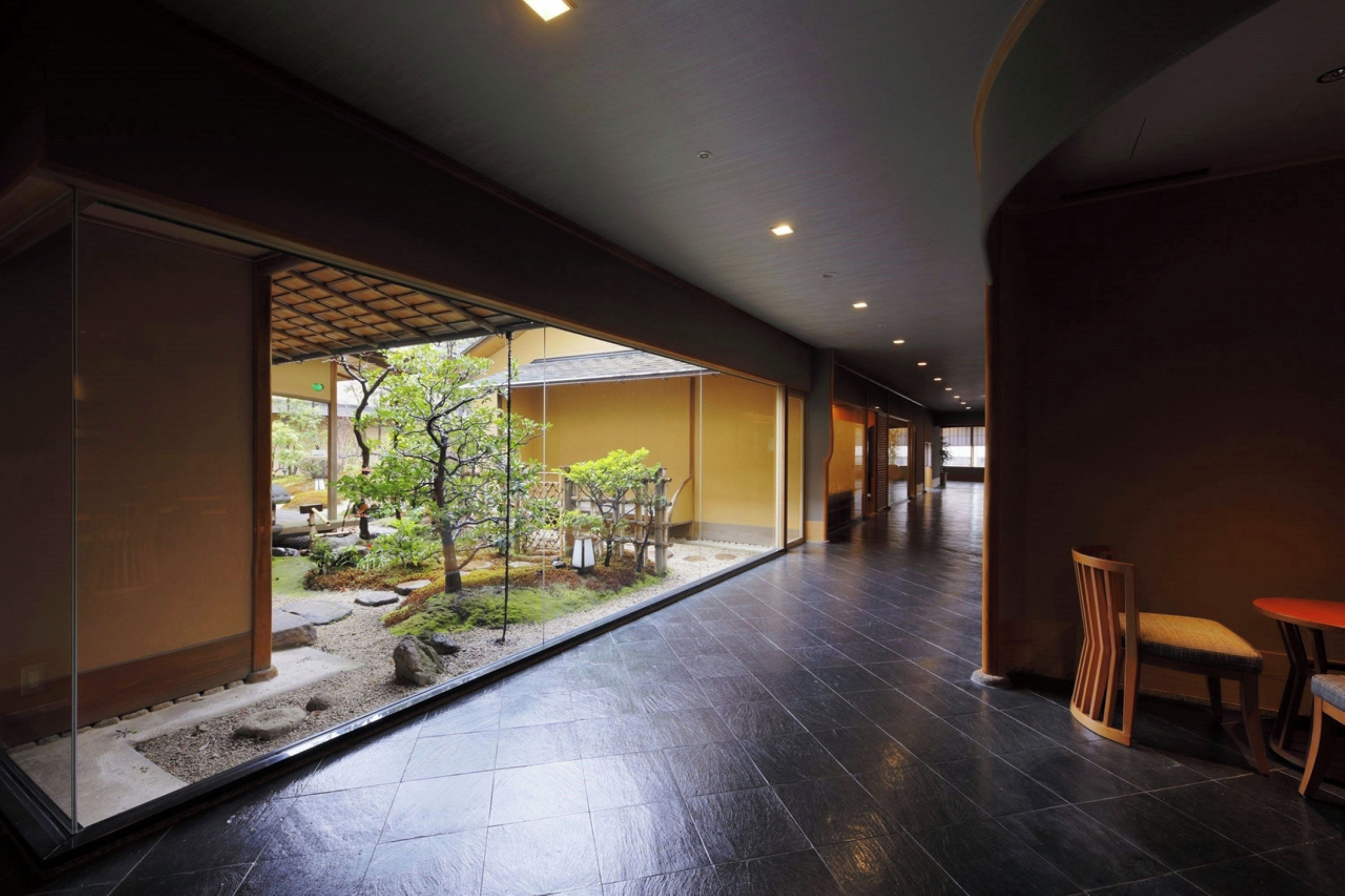 Corredor com vista para um jardim, mobiliário de madeira e piso de azulejos.