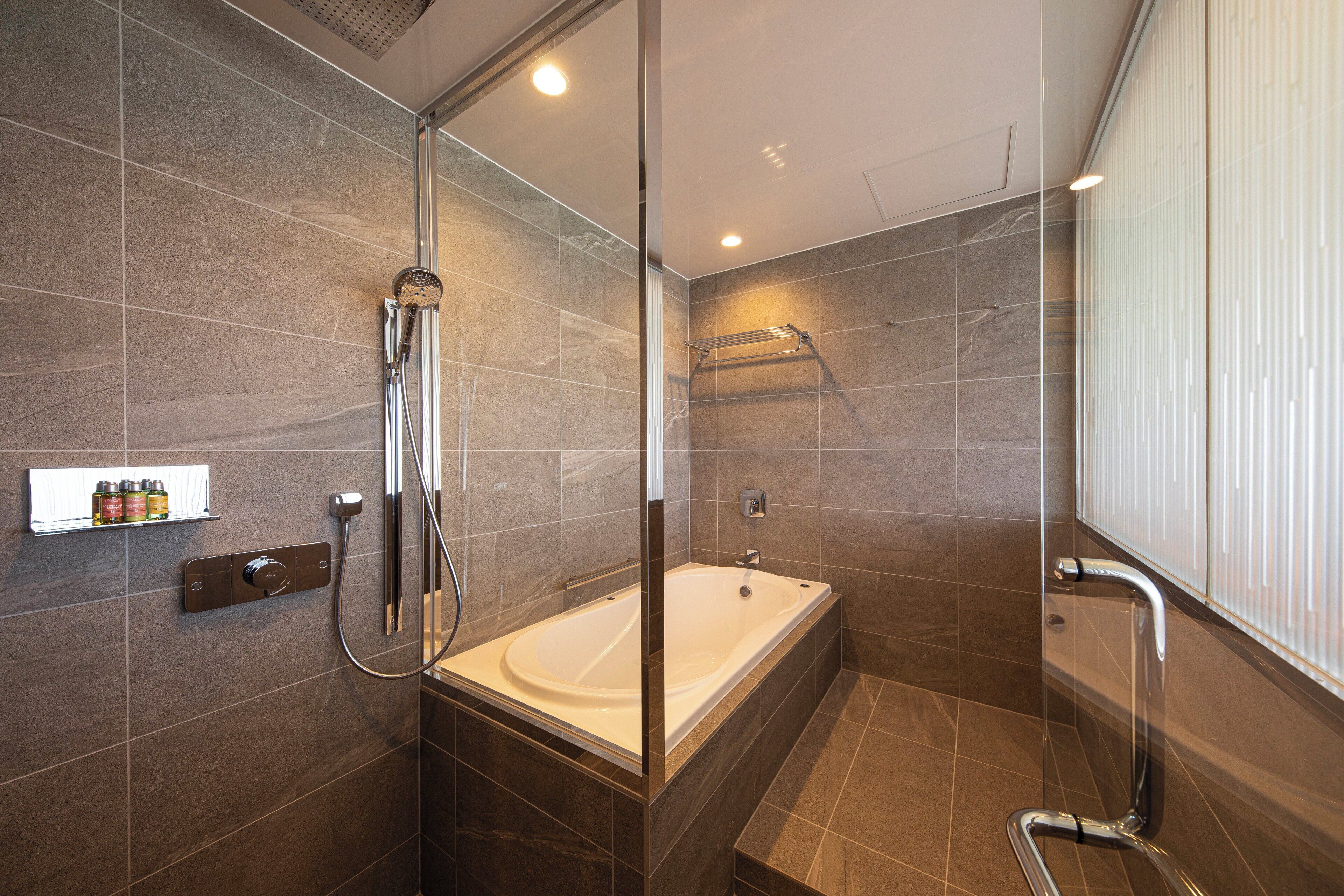 A modern bathroom with a glass-enclosed shower, a freestanding bathtub, and a wall-mounted shelf with toiletries.