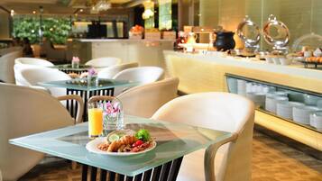 A breakfast setting with a glass table, chairs, and a buffet area in the background.