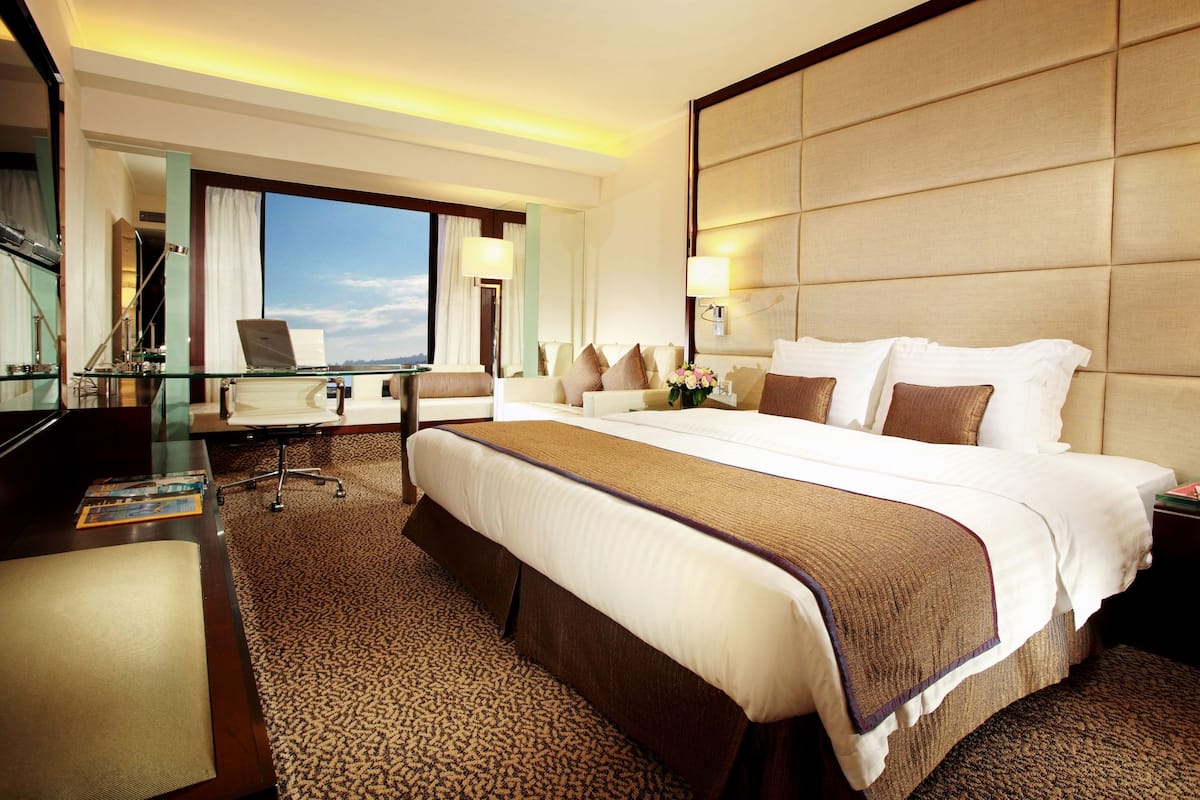 Habitación de hotel con una cama grande, un escritorio con una computadora portátil, una silla y vistas al cielo.