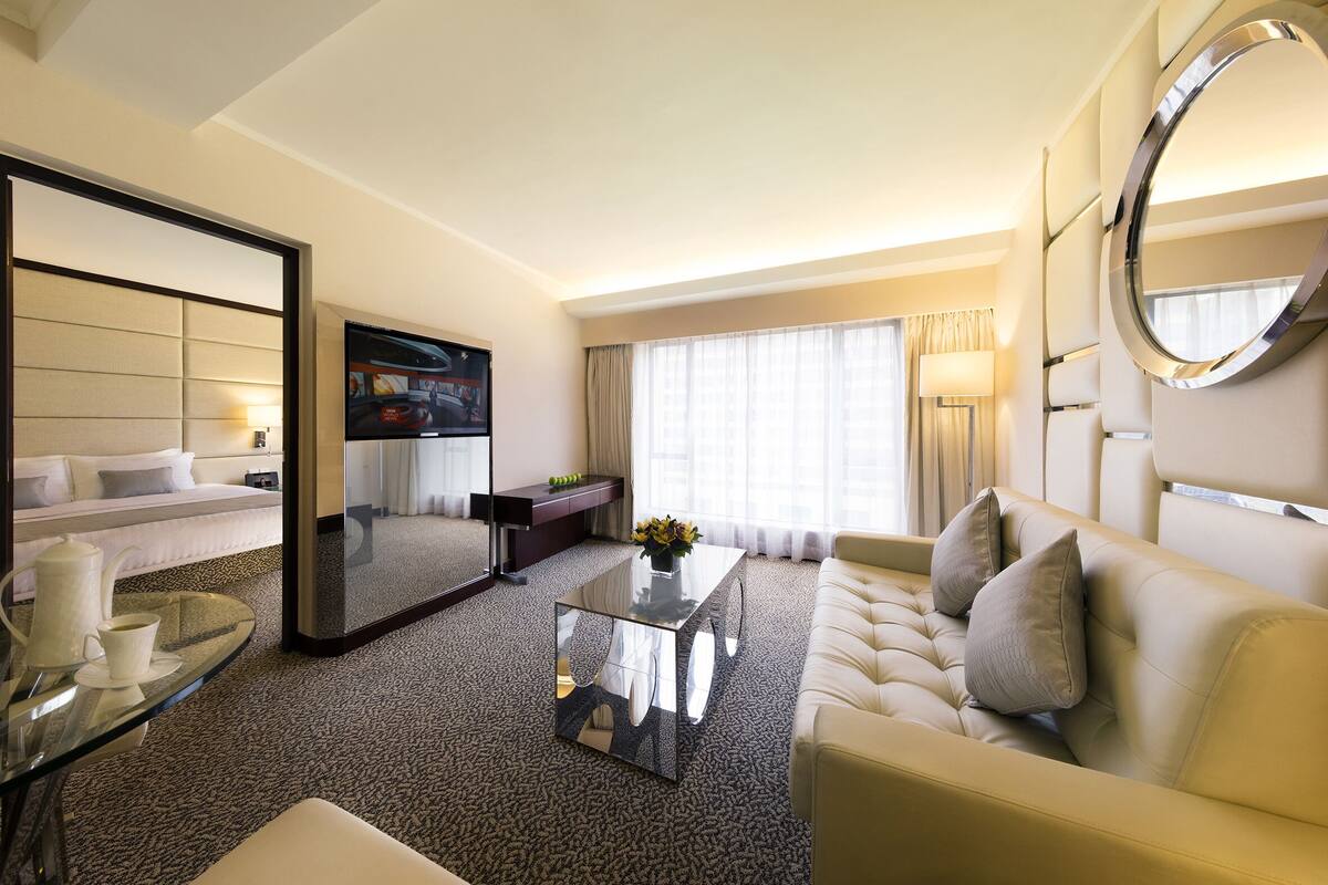 Una habitación de hotel con una cama grande, un sofá, una mesa de centro, un televisor y un espejo.