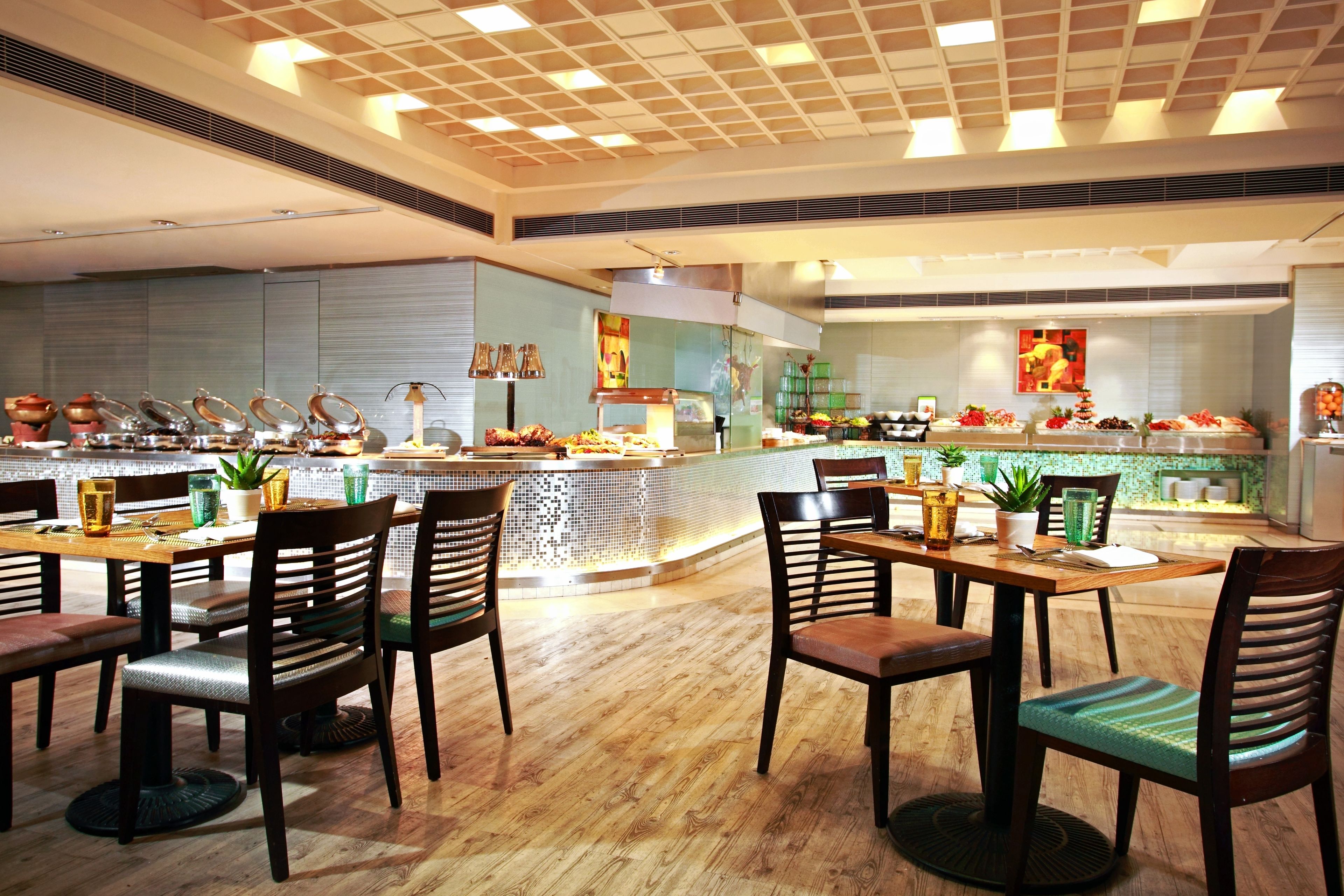 Un restaurante moderno con mesas y sillas de madera, una barra central con exhibición de alimentos y un salpicadero de azulejos.