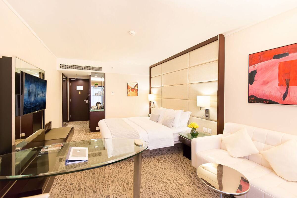 Una habitación de hotel con una cama, un sofá, una mesita de vidrio, un televisor y un cuadro en la pared.