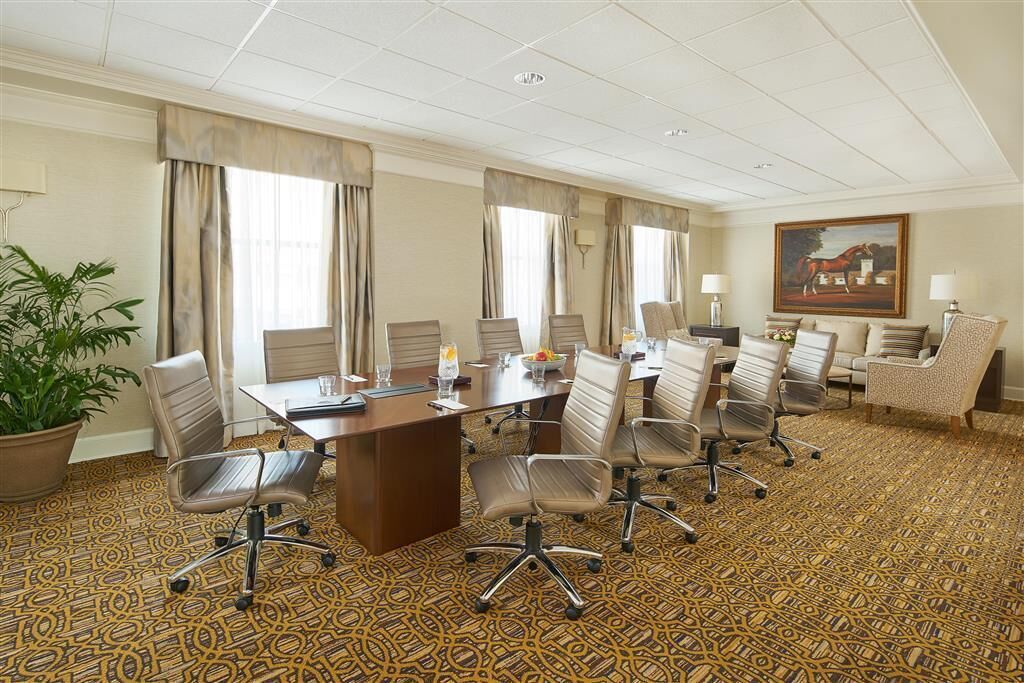 A conference room with a large table, multiple chairs, a potted plant, and a painting on the wall.