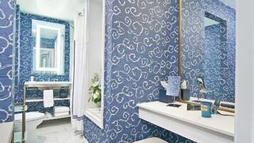 A bathroom with a blue patterned wall, a white sink, a mirror, and a bench.