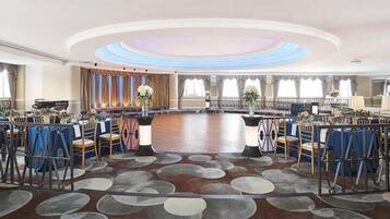 Uma grande sala de banquetes circular com chão de madeira e cadeiras azuis e brancas dispostas em volta de mesas.