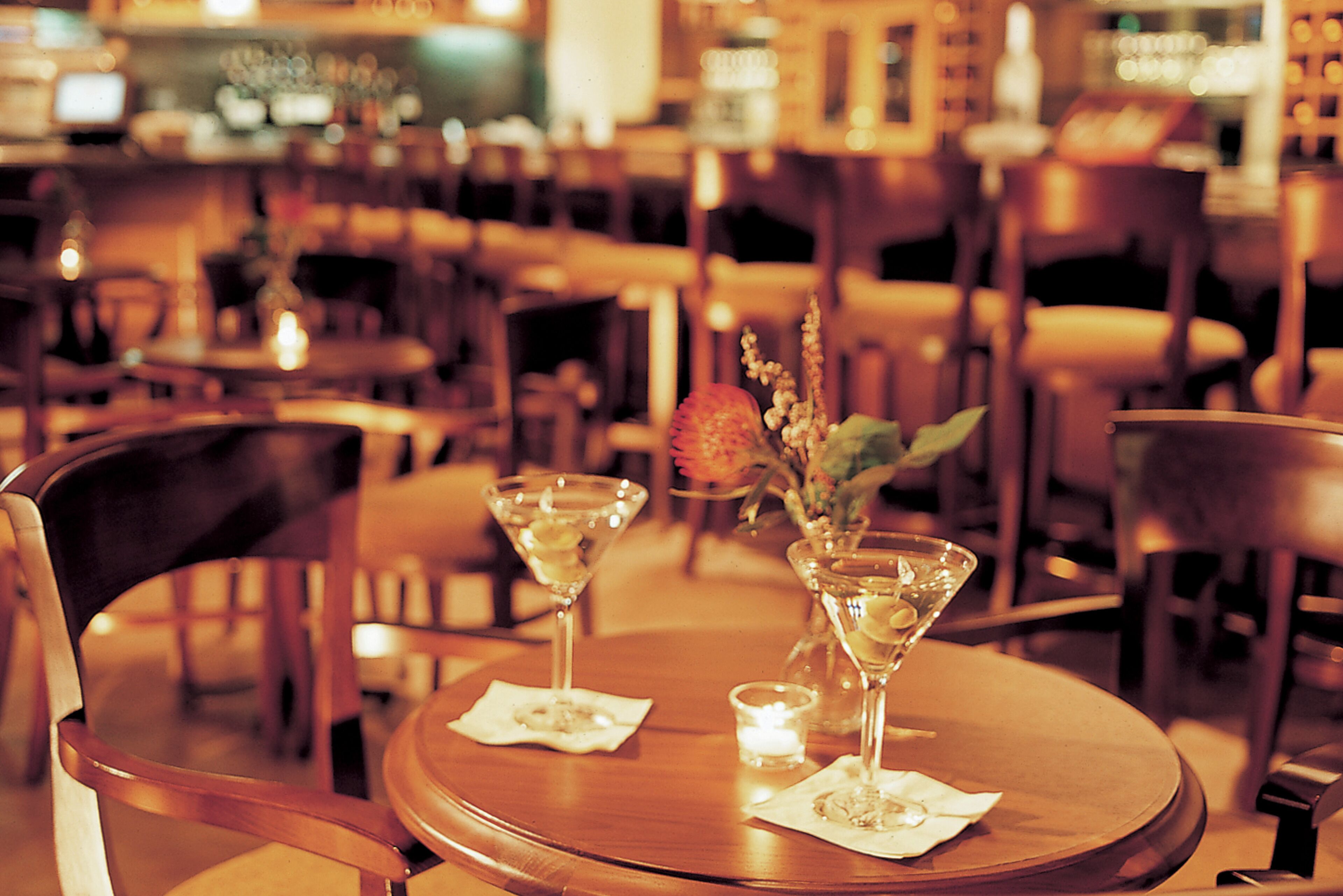 A restaurant interior with round tables, chairs, and a bar in the background.