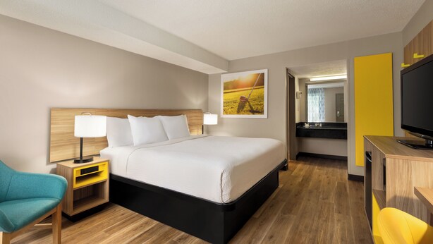 Habitación de hotel con una cama, una mesita de noche con lámpara, un escritorio con televisor y una silla.