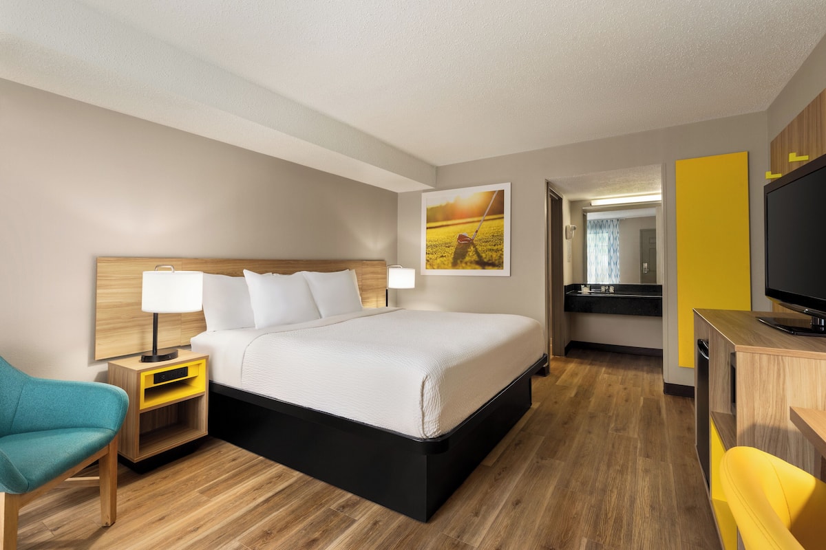 A hotel room with a bed, a nightstand with a lamp, a desk with a TV, and a chair.