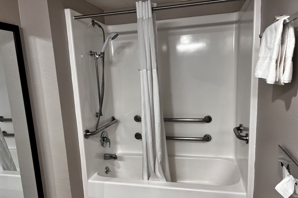 A white bathtub with a shower head, grab bars, and a curtain.