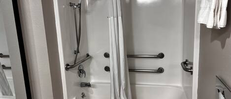 Una vasca da bagno bianca con doccetta, maniglie di sostegno e tenda.