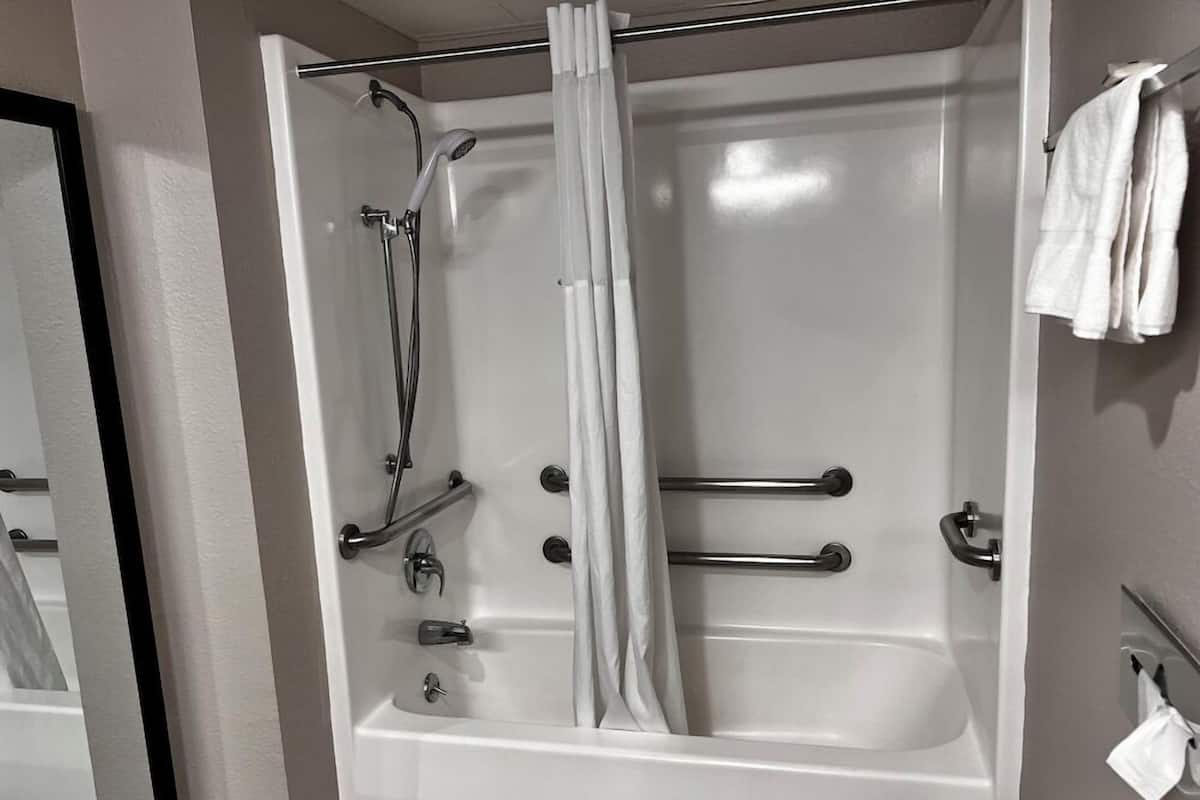 A bathroom with a bathtub, shower, and handrails.