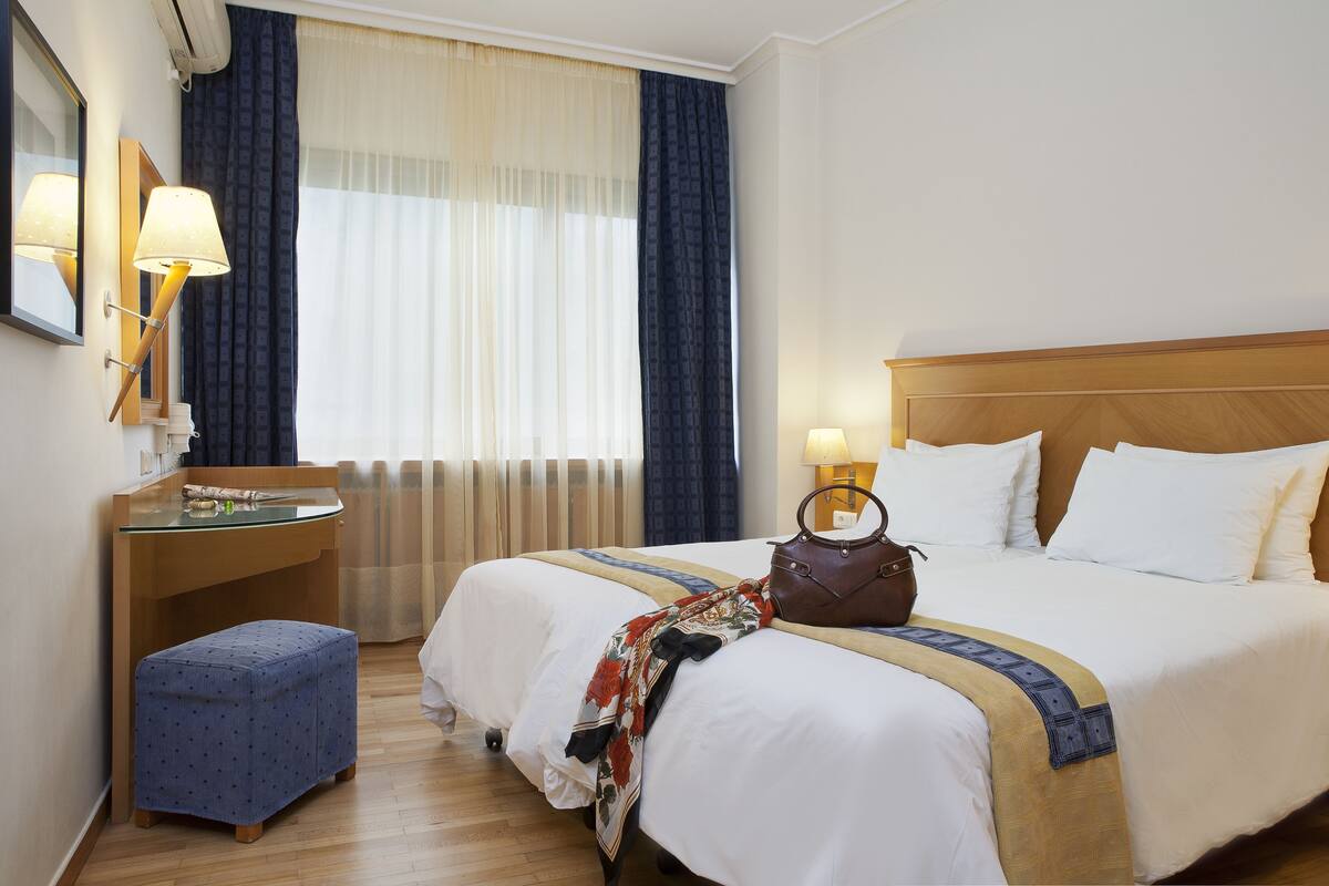 A hotel room with a bed, a desk, a chair, and a window with curtains.
