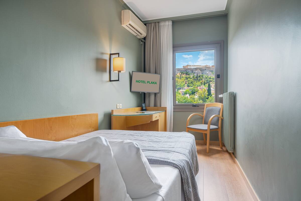 A hotel room with a bed, a desk, a chair, a TV, and a window with a view of a historic building.