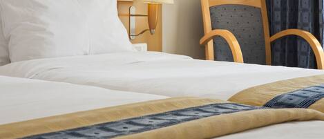 A hotel room with a bed, a nightstand with a lamp, a wooden chair, and a patterned throw blanket.