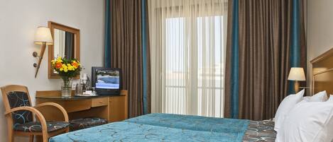 A hotel room with a bed, a desk with a computer, a chair, and a window with curtains.