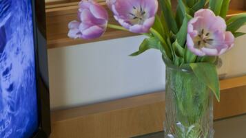 A hotel room with a bed, a bedside lamp, a framed picture on the wall, and a vase with purple tulips on the nightstand.