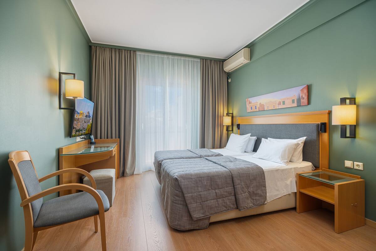 A hotel room with a bed, desk, chair, and a painting on the wall.