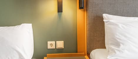 Quarto de hotel com duas camas, mesa de cabeceira com abajur e um quadro na parede.