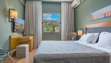 Quarto de hotel com cama, escrivaninha, cadeira, janela com vista para um edifício histórico e um quadro na parede.